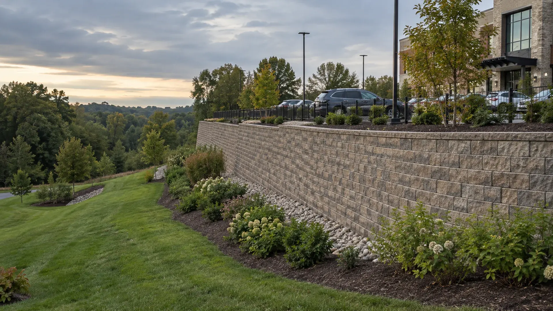 A long engineered segmental block retaining wall along a new commercial development, parking lot above and landscaped slope below.