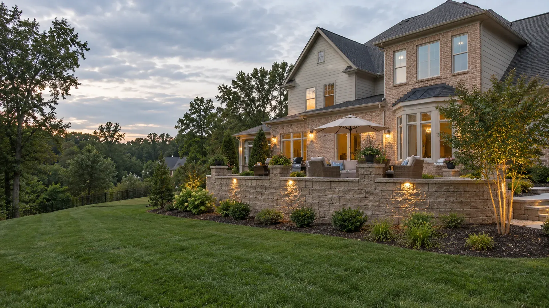 A newer large brick-and-siding home in Short Pump, Virginia with a premium tan block retaining wall and landscape lighting framing a raised patio.